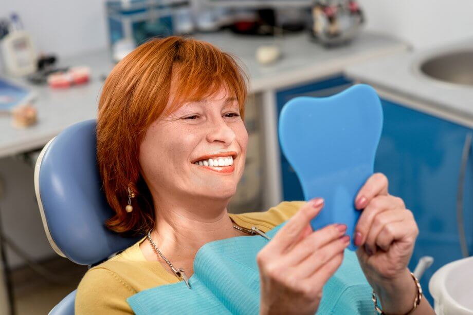 Woman Smiling In Hand Held Mirror After Dental Implants