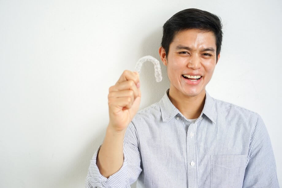 Man wearing a button down shirt, smiling and holding an Invisalign aligner.