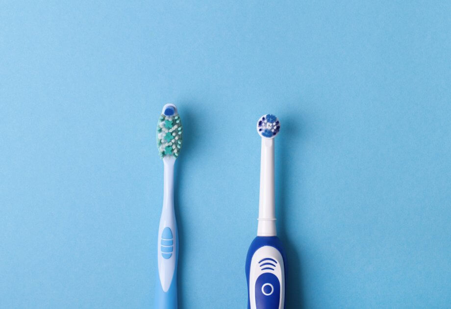 Photograph of a blue manual and a blue electric toothbrush side-by-side in front of a light blue background.