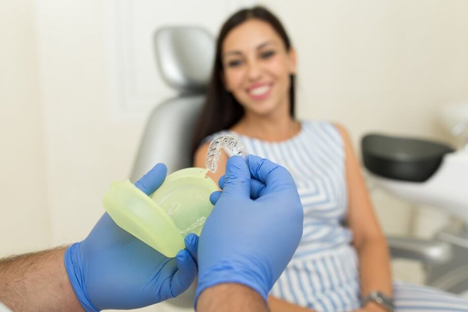 dentist's hands holding Invisalign with patient in background
