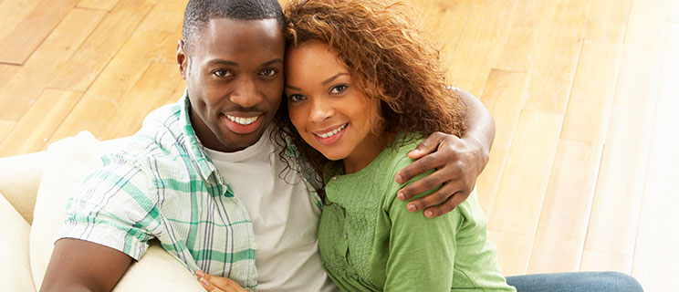 young couple sitting on couch, hugging and smiling