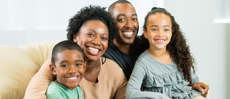 Mom, Dad son and daughter sitting on couch, smiling