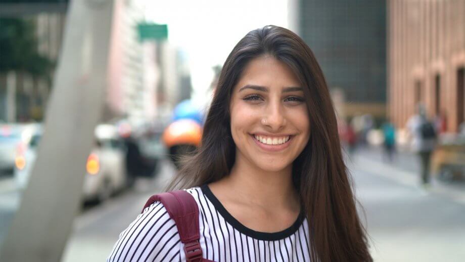 young smiling woman standing on city sidewalk